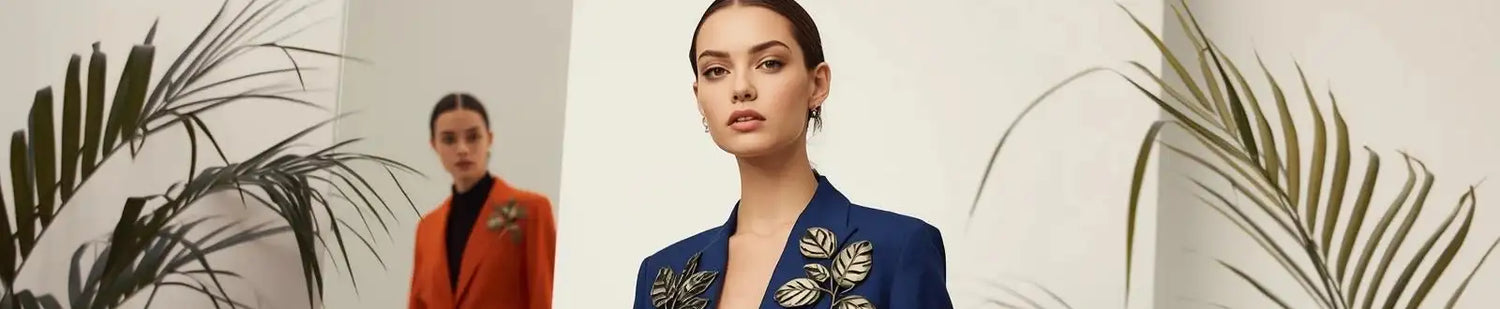 Two women in stylish suits with decorative elements, one in blue and the other in orange, against a neutral background with leafy decorations.